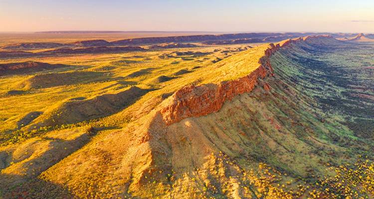 Goudkleurig luchtfoto van een lange, ruige bergrug die zich uitstrekt over het rode hart van Australië