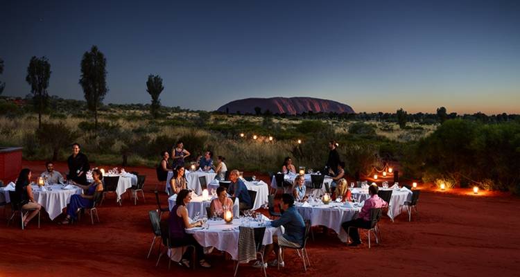 Elegant buitendiner in het schemerlicht op rood woestijnzand met Uluru als silhouet aan de horizon