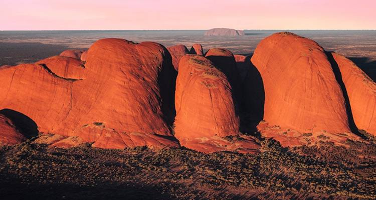 Luchtfoto van zonsopgang met de massieve ronde koepels van Kata Tjuta die uit de outback vlakte omhoog rijzen