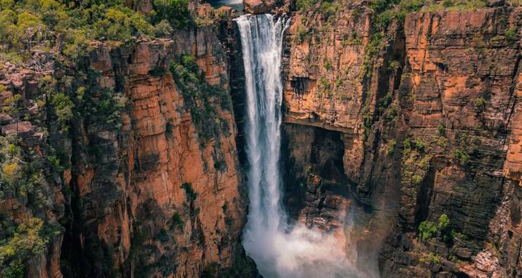 Vista aérea espectacular de una cascada alta cayendo por acantilados de arenisca roja hacia una piscina brumosa