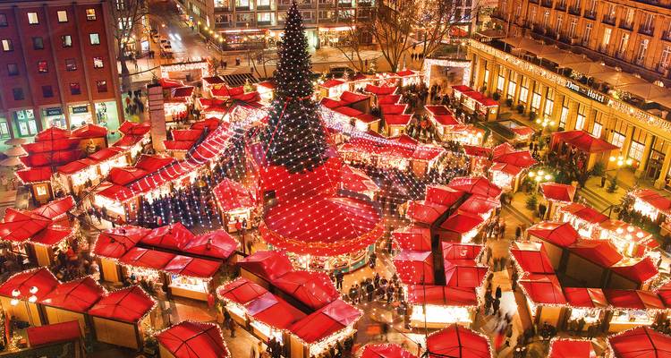 Lebendige Luftaufnahme eines weihnachtlichen Stadtmarkts mit Reihen von rotgedeckten Ständen, die unter festlicher Beleuchtung leuchten.