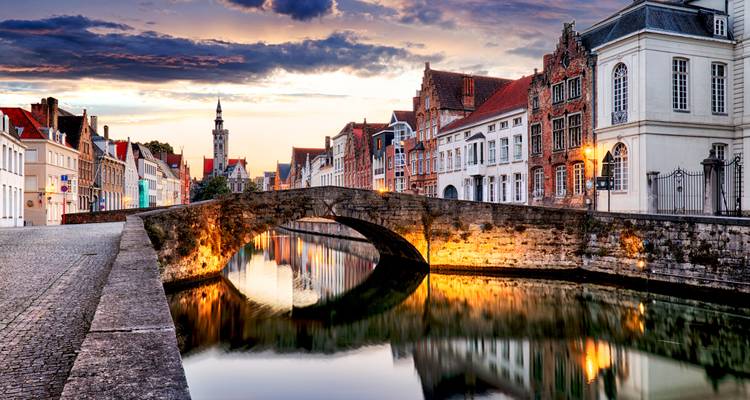 Malerische Steinbrücke, die sich in einem Kanal bei Einbruch der Dunkelheit im historischen Zentrum von Brügge spiegelt