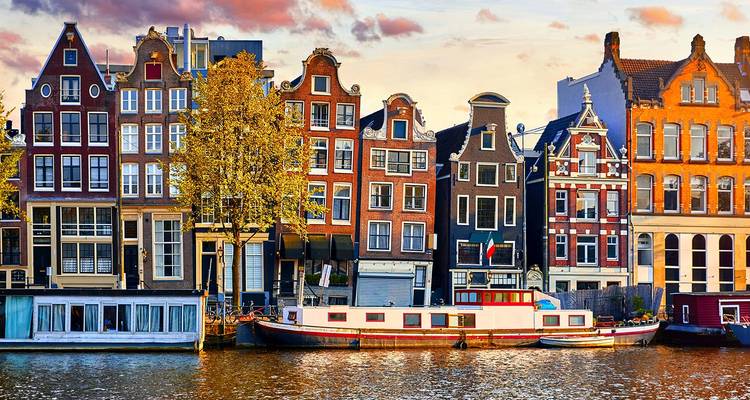 Les maisons à pignons iconiques le long d'un canal d'Amsterdam et une péniche amarrée au coucher du soleil.