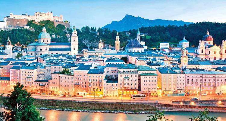 Panoramisch avondaanzicht over Salzburgs oude stad, fort en rivier met bergen op de achtergrond.