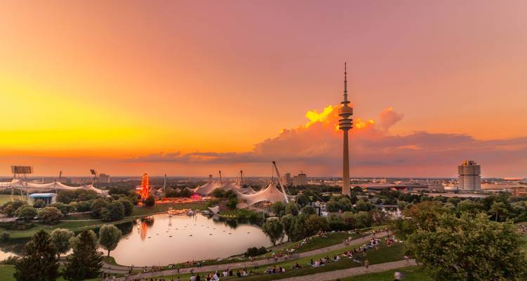 Zonsondergang boven het meer van Münchens Olympiapark met toren en menigtes op de grasige oevers