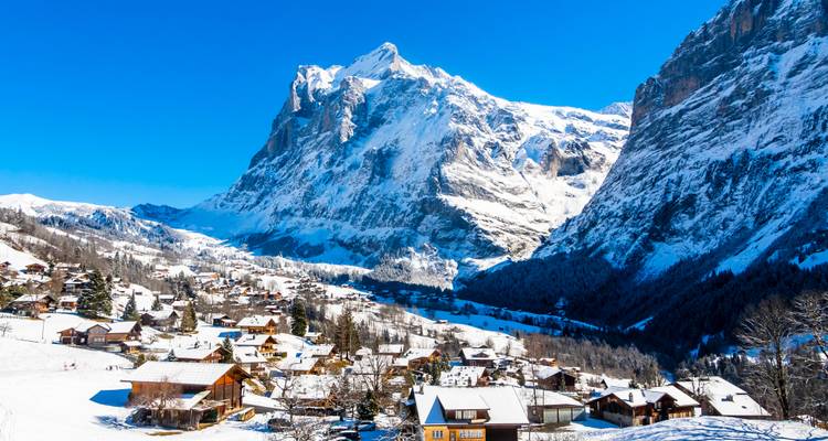 Village alpin enneigé dominé par le majestueux pic de l'Eiger illuminé par le soleil sous un ciel d'hiver d'un bleu cristallin.