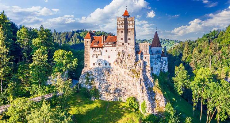 Vue aérienne spectaculaire du château de Bran perché sur une colline rocheuse entourée d'une forêt luxuriante.