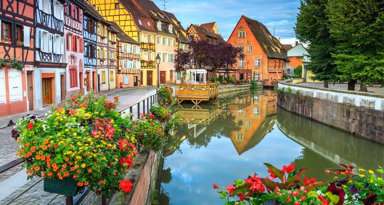 Farbenfrohe Fachwerkhäuser und lebendige Blumenkästen säumen einen ruhigen Kanal, der sich wie ein Spiegel in Colmars Klein-Venedig widerspiegelt.