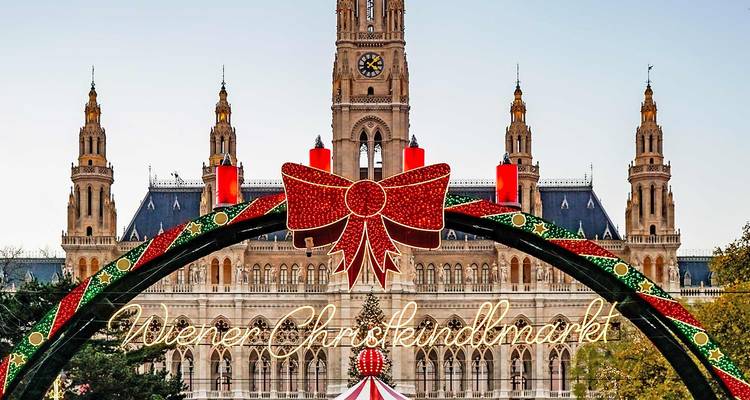 Arco festivo con el texto "Wiener Christkindlmarkt" frente al ornamentado Rathaus de Viena al atardecer.