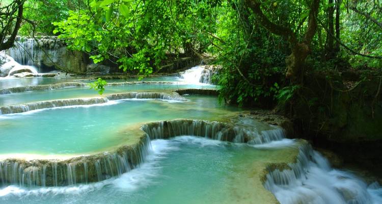 Die türkisfarbenen Terrassen-Pools des Kuang Si Wasserfalls fließen sanft durch dichten Dschungel.