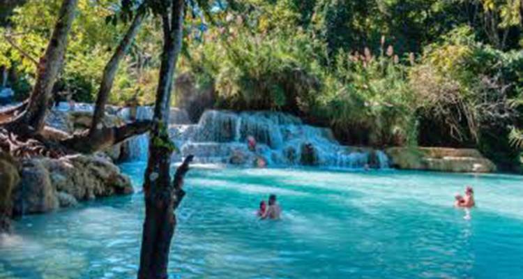 Besucher schwimmen und waten in einem leuchtend türkisfarbenen Wasserfallbecken, das von Wald umgeben ist.