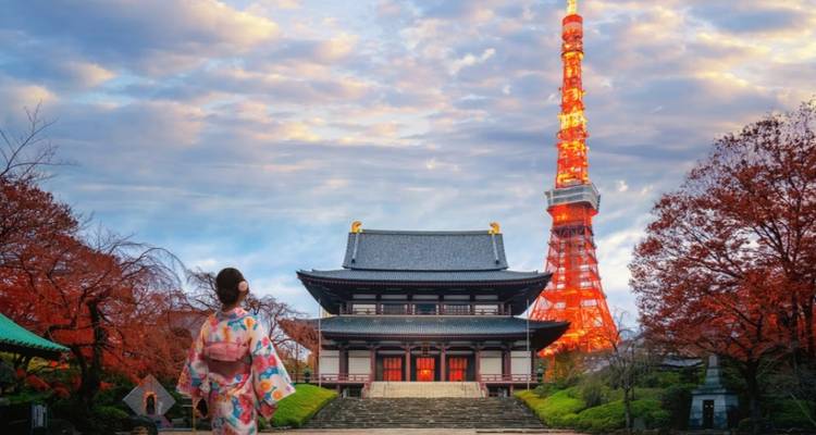 Frau in farbenfrohem Kimono bewundert den Zojo-ji-Tempel mit dem beleuchteten Tokyo Tower in der Dämmerung inmitten von Herbstlaub.