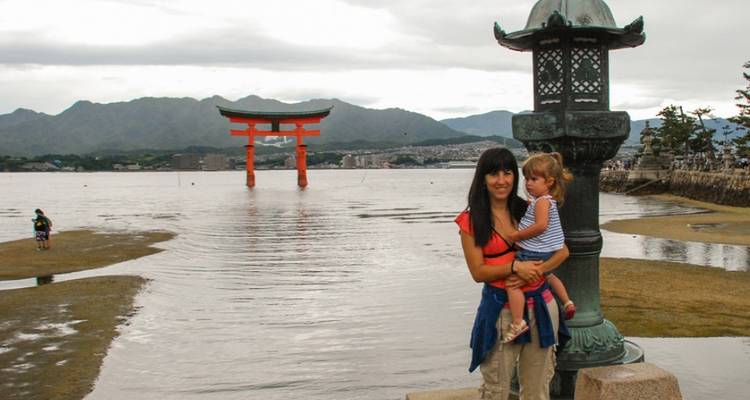 Mutter, die ihr Kind vor dem berühmten schwimmenden Torii-Tor auf der Insel Miyajima haelt.
