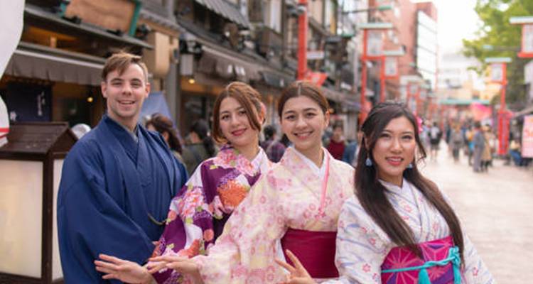 Gruppe von Freunden in farbenfrohen Kimonos, die sich in einer traditionellen Einkaufsstraße in Pose setzen.