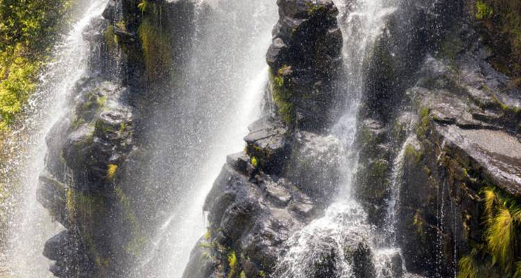 Gros plan d'une cascade multi-étages s'écoulant sur des roches sombres avec brume et embruns.