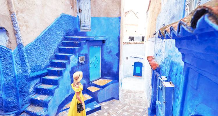 Voyageur en robe jaune explorant les ruelles et escaliers bleu vif de la médina de Chefchaouen