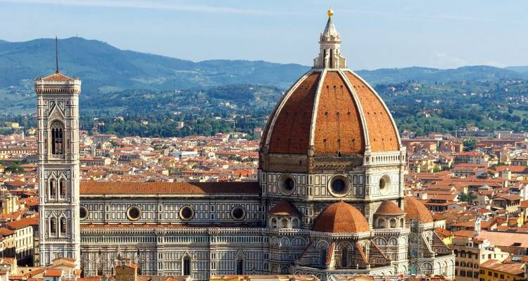 Een helder panoramisch uitzicht op Florence met de iconische kathedraal met rode koepel die boven een zee van terracotta daken uitstijgt met verre heuvels onder een blauwe lucht.