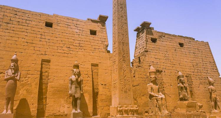 Fachada de piedra arenisca del complejo del Templo de Karnak en Luxor con un obelisco alto y estatuas sentadas.