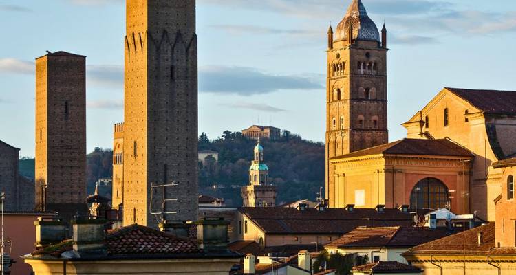 Historische bakstenen torens en kerktorens van Bologna die warm zonsonderganglicht opvangen boven dakpannen.