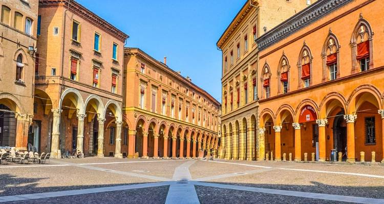 Kleurrijke gebouwen met arcaden rond een rustig plein in Bologna onder een heldere blauwe lucht.