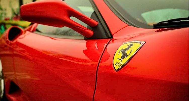 Close-up van een felrode Ferrari sportwagen met het iconische springende paard logo op de voorgrond.