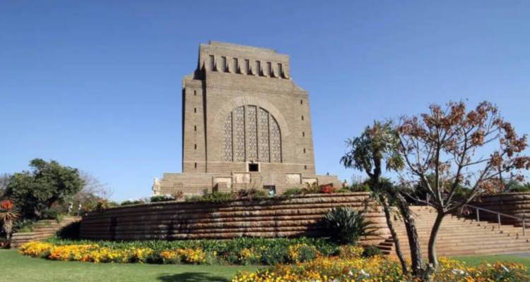 Monument colossal Voortrekker en pierre, entouré de jardins en terrasses et de parterres de fleurs colorés sous un ciel dégagé