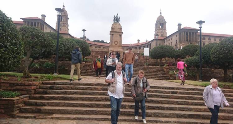 Des visiteurs descendant les marches en pierre devant le complexe des Union Buildings lors d'une journée nuageuse
