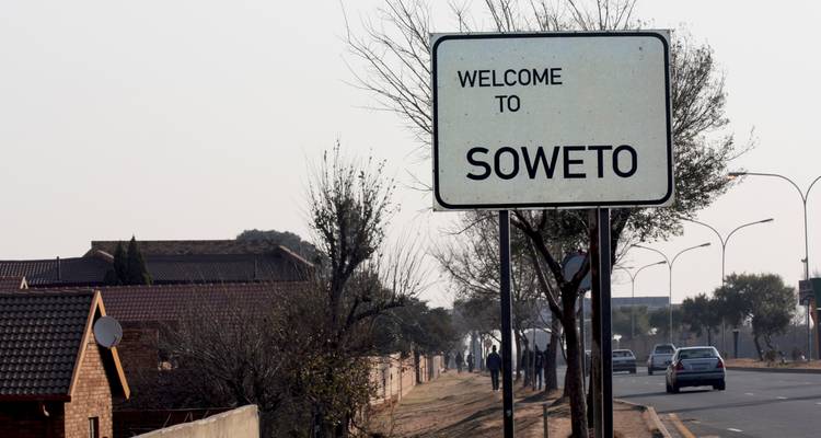 Panneau routier affichant « Bienvenue à Soweto » le long d'une rue de banlieue avec des voitures et des piétons