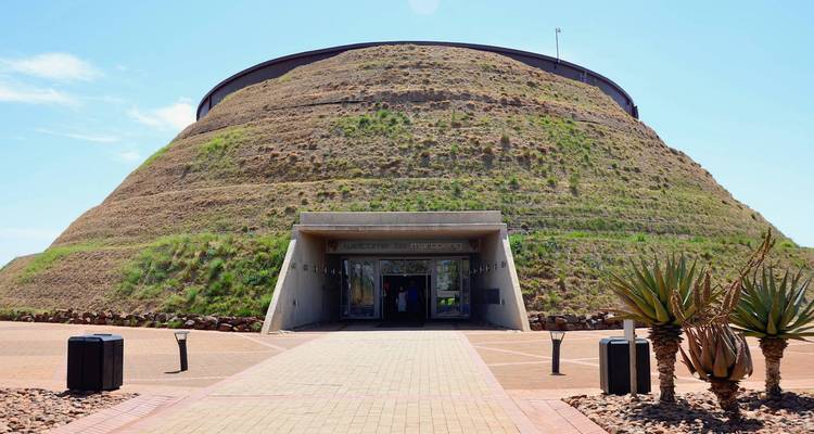 Entrée du Centre des visiteurs de Maropeng en forme de monticule couvert de gazon avec un portail en béton moderne sous un ciel bleu