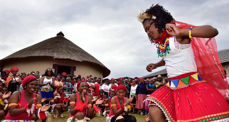 Performance de danse traditionnelle sud-africaine vibrante devant une hutte au toit de chaume observée par une large foule