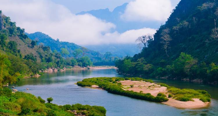 Amplia vista panorámica de un río sinuoso flanqueado por exuberantes montañas verdes bajo nubes brumosas.