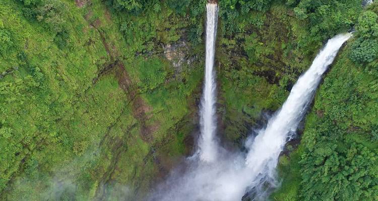 Vista aérea de dos espectaculares cataratas gemelas cayendo por un acantilado vertical de selva tropical hacia la niebla de abajo.
