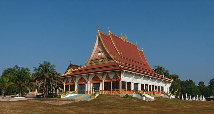 Templo budista ornamentado y aislado con techo rojo y dorado se alza en un terreno abierto bajo un cielo despejado.