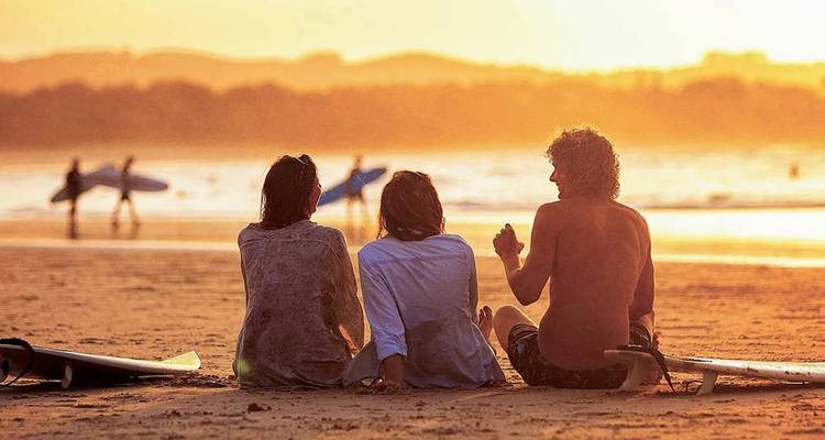 Scène en double d'amis se détendant sur une plage dorée au coucher du soleil avec des surfeurs en arrière-plan.
