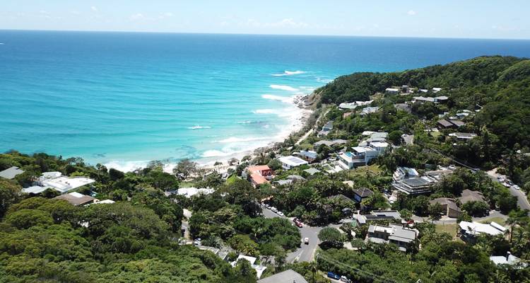 Vue aérienne des eaux turquoise et des falaises verdoyantes qui s'incurvent autour d'une ville côtière, probablement Byron Bay.