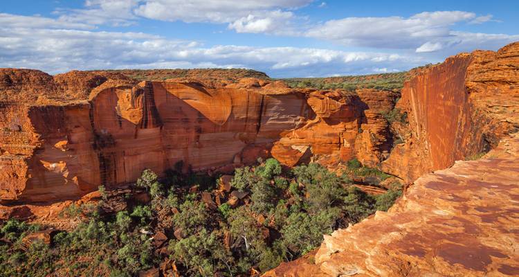 Les imposants murs de roche rouge du Kings Canyon surplombant une vallée verdoyante sous un ciel d'un bleu éclatant.