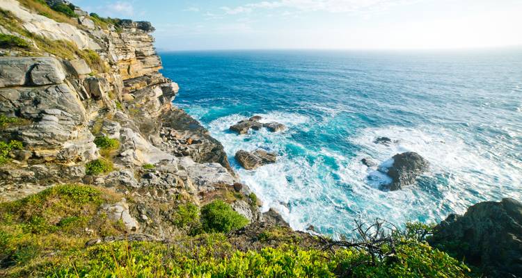 Des falaises côtières escarpées dominant les vagues déferlantes le long d'un littoral ensoleillé.
