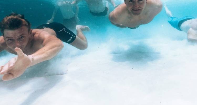 Gruppe junger Maenner beim Unterwasserschwimmen ueber weissem Sand in klarem blauem Meer