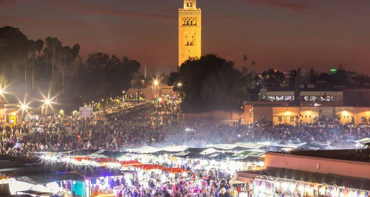 Panorama nocturne du marché Jemaa el-Fnaa de Marrakech animé par les lumières et les foules sous la Mosquée Koutoubia illuminée.