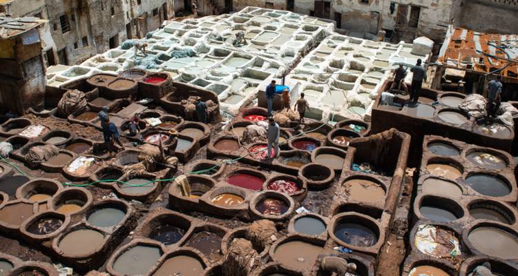 Vue en plongée de la tannerie de Fès avec des ouvriers traitant les peaux dans des cuves en pierre multicolores.
