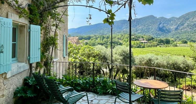 Shaded stone terrace with green metal chairs overlooking vineyards, olive trees and rolling Provencal mountains