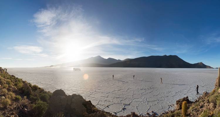 Weites Panorama der blendend weißen Salzebenen von Uyuni mit entfernten Personen und Bergen.