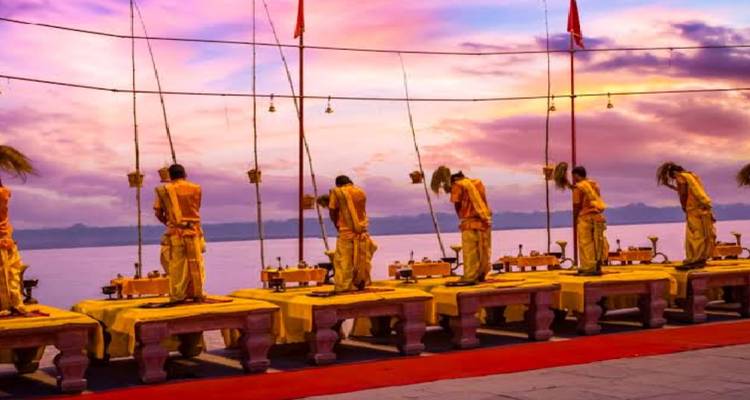 Los sacerdotes realizan el ritual Ganga Aarti en plataformas elevadas al atardecer bajo un cielo de un intenso púrpura anaranjado.
