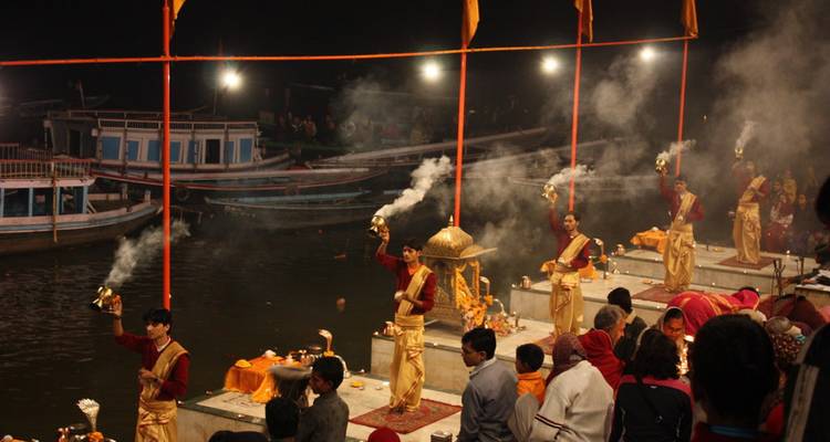 Ganga Aarti nocturno con sacerdotes sosteniendo lámparas humeantes mientras los devotos observan desde la orilla del río.