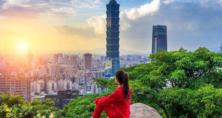 Eine Frau in Rot blickt auf die Stadt Taipei und das Taipei 101 während eines leuchtenden Sonnenuntergangs.