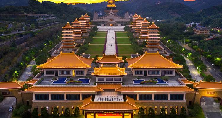 Das beleuchtete Fo Guang Shan Buddha Museum Komplex in der Abenddämmerung mit Bergen im Hintergrund.