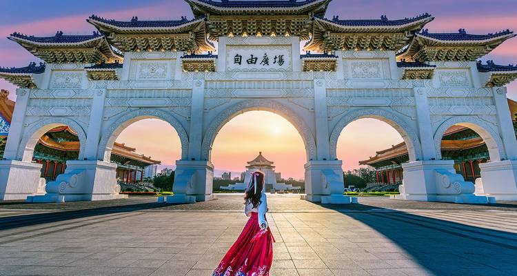 Woman in red dress walks toward ornate Liberty Square Arch at dawn.