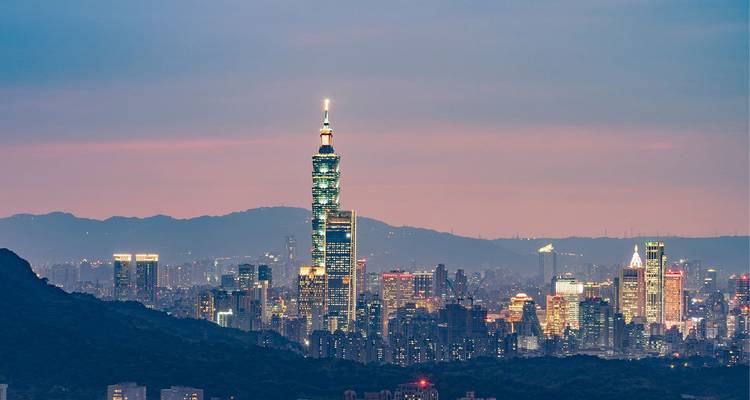 Dusk view of Taipei skyline with illuminated Taipei 101 against pinkish sky.