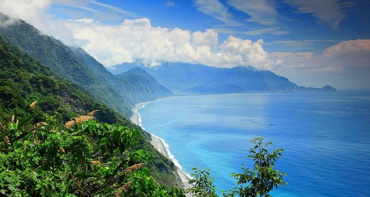 Dramatic coastal cliffs covered in lush greenery beside vivid blue Pacific waters.