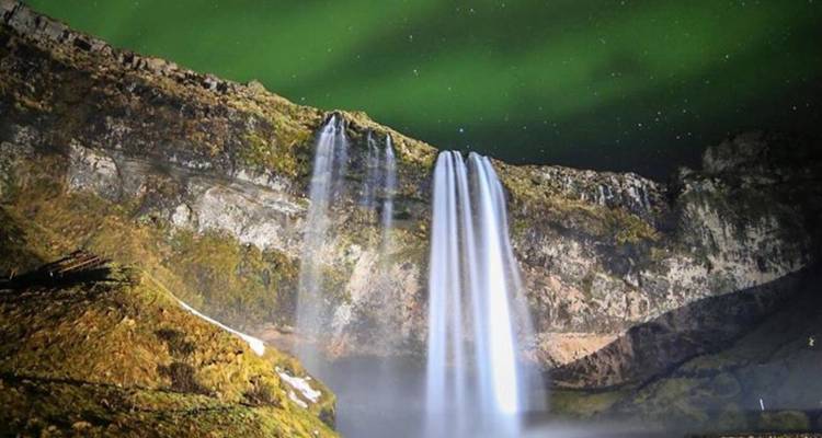 Les aurores boréales scintillent au-dessus de la cascade de Seljalandsfoss qui dégringole d'une falaise la nuit.